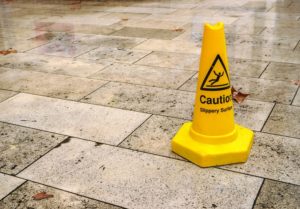 yellow cone with caution slippery surface sign, on wet pavement tiles.