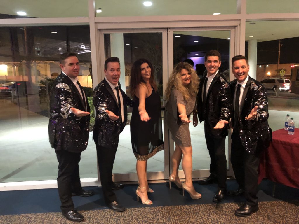 Angela Zervos and Lauren Calta posing with entertainers wearing shiny jackets