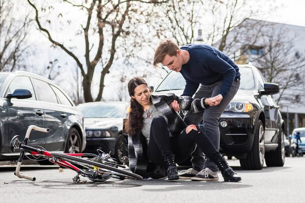 Young man helping the woman cyclist from bicycle accident.