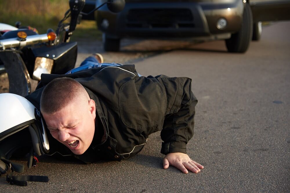 Motorcycle rider in pain after collision with car on the road.