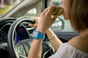 Woman driver eating sandwich while driving.
