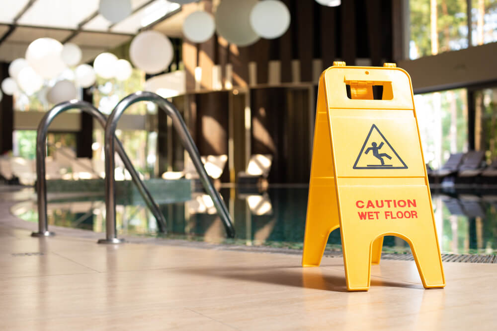 Yellow sign of warning wet floor plate is near the swimming pool.