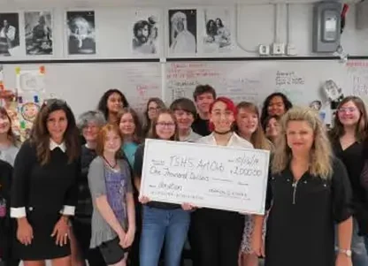 Group of people standing in a classroom holding a large check for $2000 made out to TSHS AMOR.