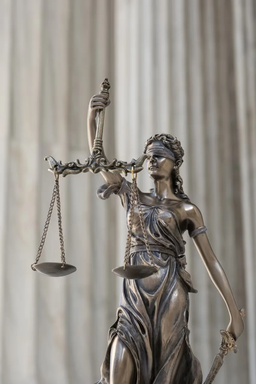 Bronze statue of Lady Justice blindfolded, holding balanced scales in one hand and a sword in the other.